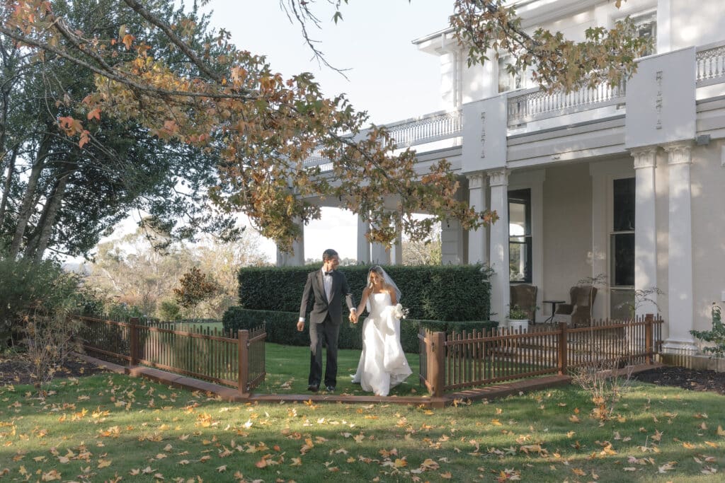 Couple celebrating a destination wedding in the gardens at Calstock Estate, a historic Tasmania wedding venue, with guests enjoying drinks near the homestead